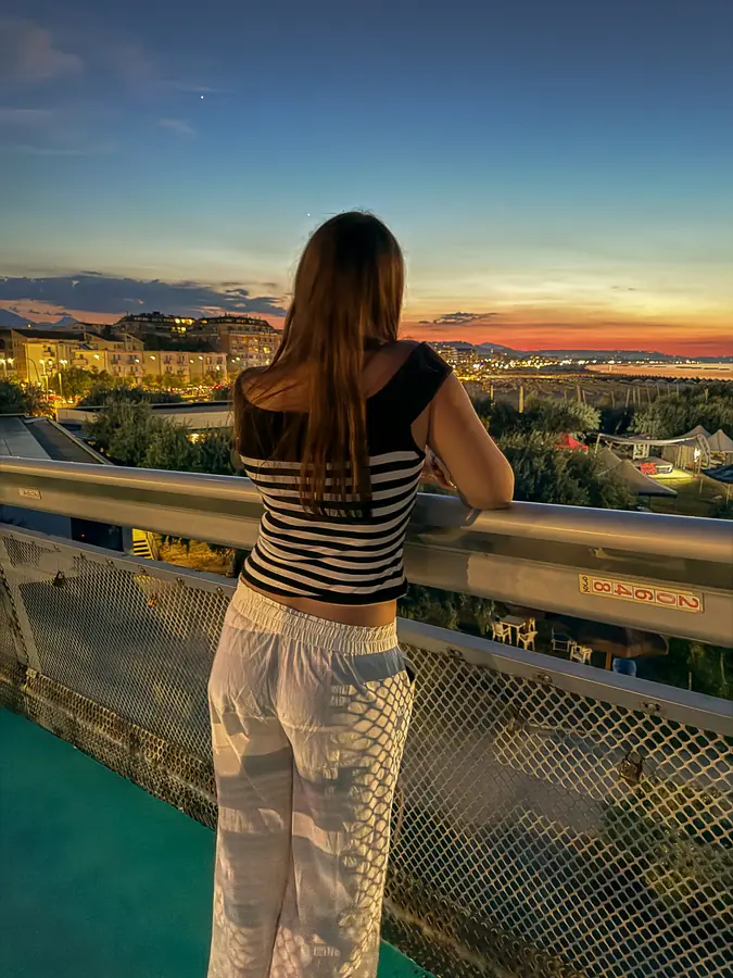 Una ragazza di spalle guarda il crepuscolo dal parapetto del Ponte del Mare